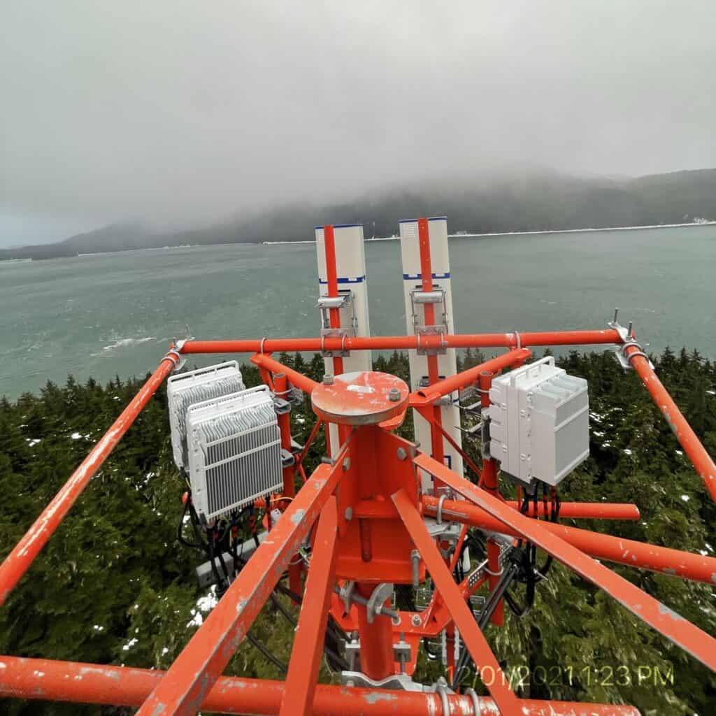 A cellular piece of equipment sits atop a mountain, with rain, mountains, and ocean in the background.