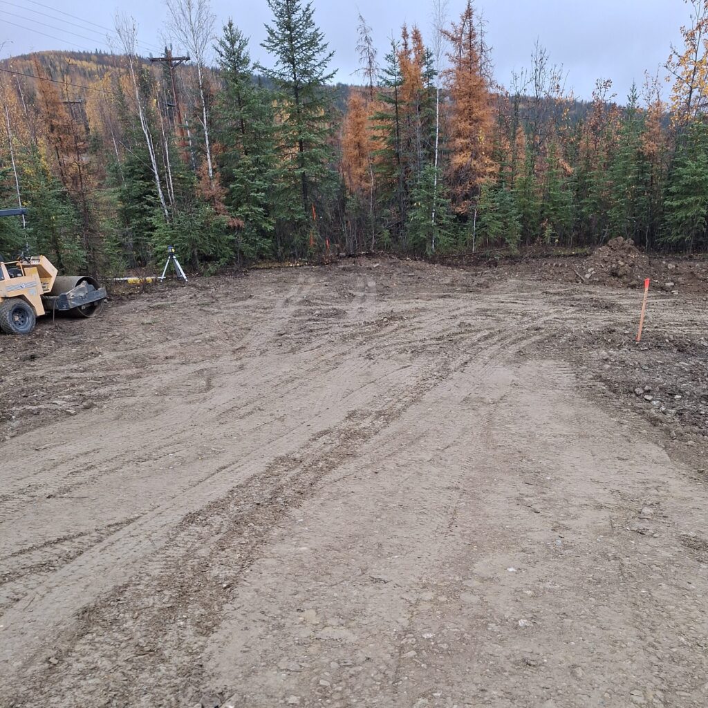 A dirt lot with evergreen trees and colorful orange deciduous trees in the background.